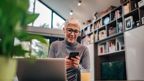 Woman in front of a Laptop holding a Smartphone.